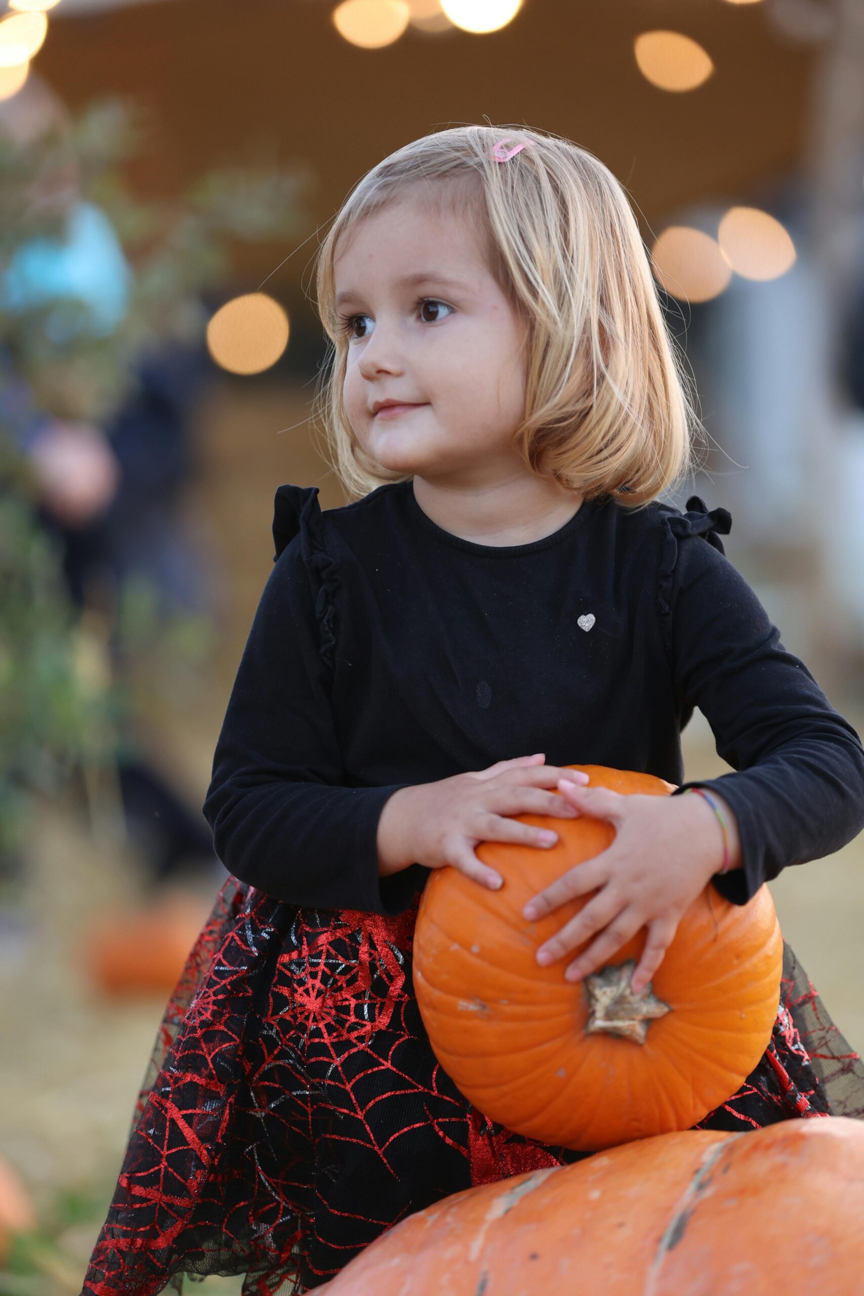 Cute girl in a Halloween dress hugs a pumpkin with a joyful expression, perfect for festive themes.